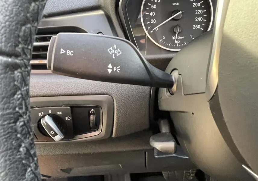 Gros plan sur la manette de clignotant à gauche du volant d'une BMW Série 2 Gran Tourer F46 noire, tableau de bord visible.