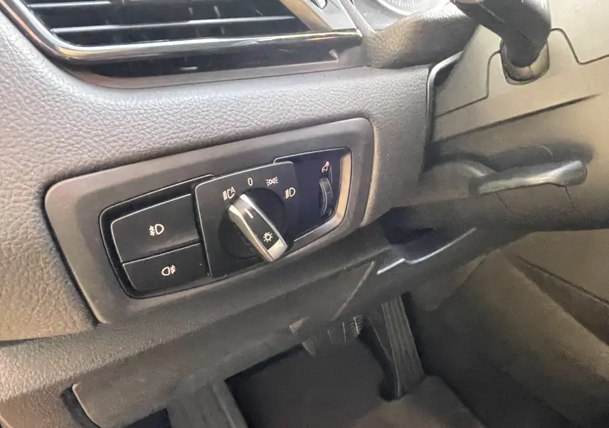 Gros plan sur le tableau de bord côté gauche d'une BMW Série 2 Gran Tourer noire, montrant la commande des phares.