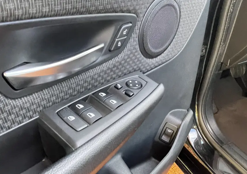 Gros plan sur la porte côté gauche d'une BMW Série 2 Gran Tourer noire, montrant les commandes des vitres et la poignée intérieure.