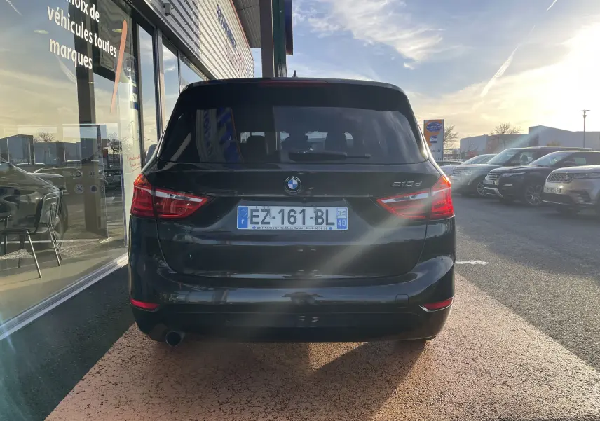 Vue arrière d'une BMW Série 2 Gran Tourer 218d noire, stationnée devant une vitrine en fin d'après-midi.