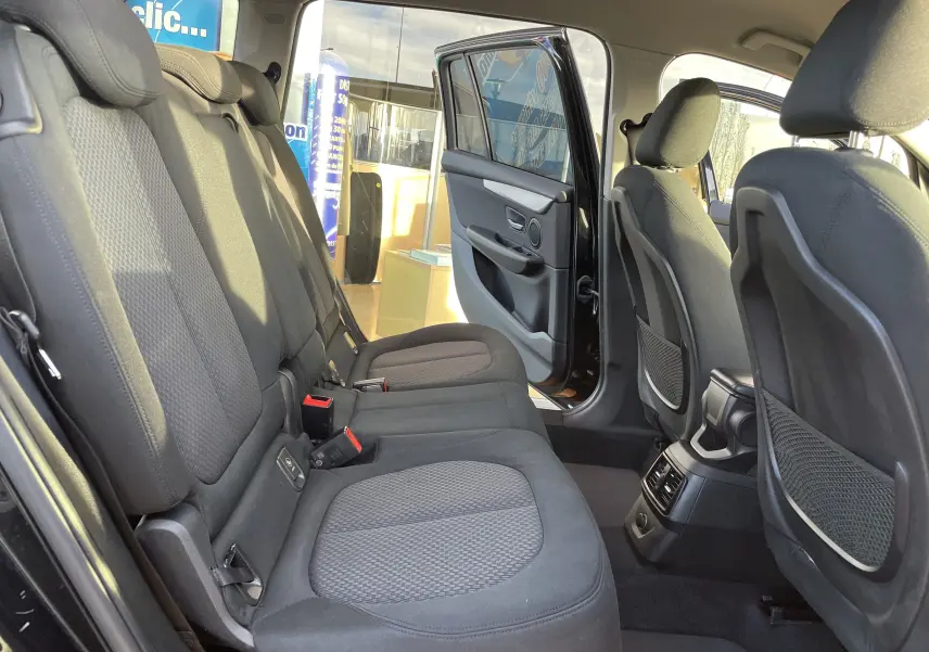 Intérieur arrière de la BMW Série 2 Gran Tourer 218d noire, vue côté gauche avec portes ouvertes et sièges en tissu gris.
