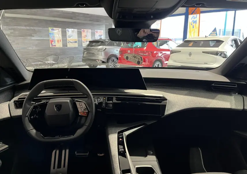 Vue intérieure avant du Peugeot 3008 gris titanium 2025, mettant en valeur le volant compact et l'écran panoramique incurvé.
