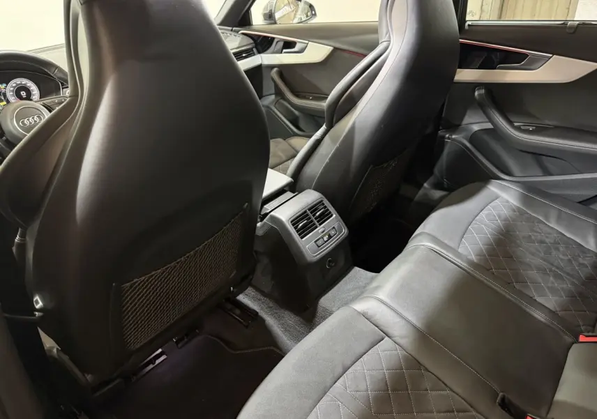 Vue intérieure arrière de l'Audi A4 gris foncé, montrant les sièges en cuir et la console centrale avec ventilation.