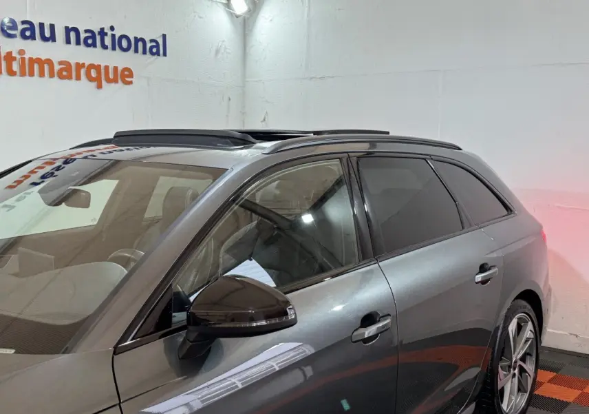 Vue de profil côté gauche d'une Audi A4 gris foncé avec toit ouvrant panoramique en intérieur showroom.