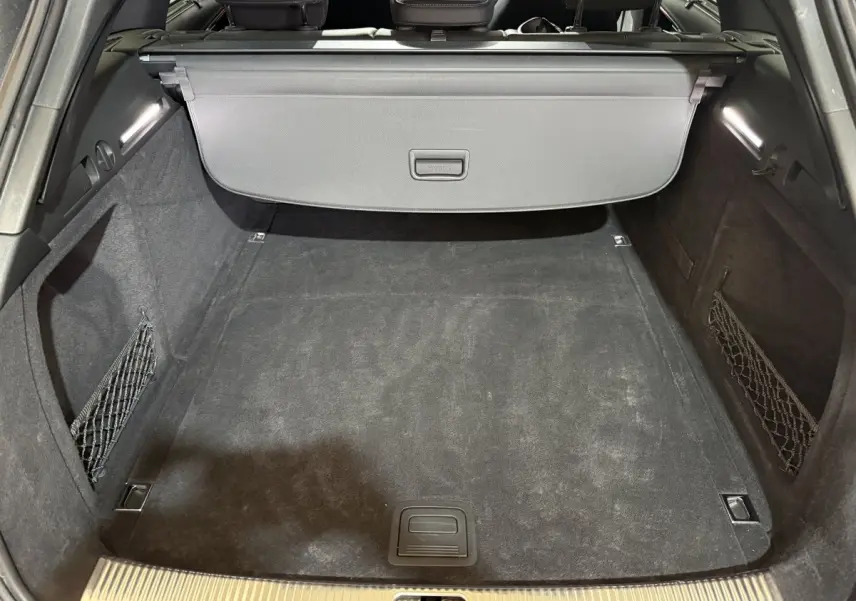 Coffre vu de face, intérieur noir avec filet de rangement latéral, cache-bagages et éclairage LED, Audi A4 gris foncé.