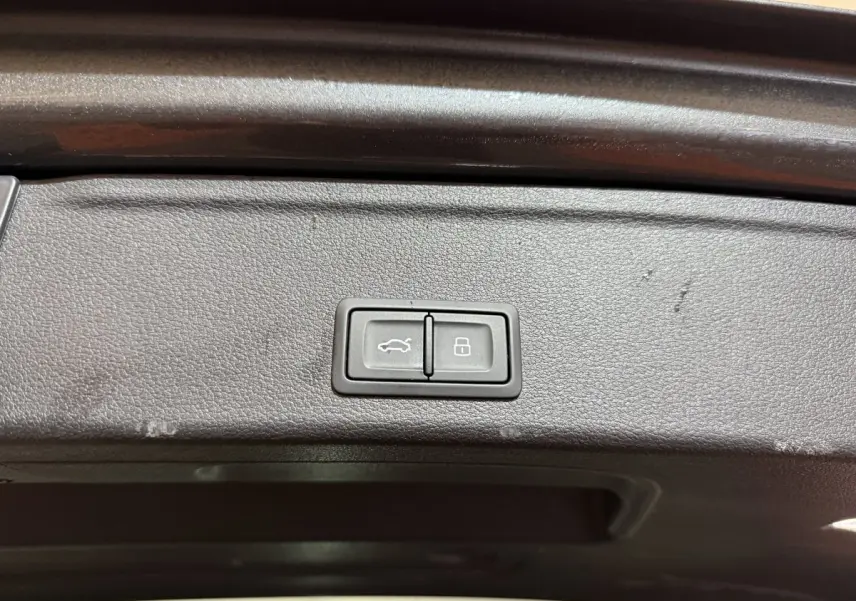 Gros plan sur les boutons d'ouverture et de verrouillage du coffre d'une Audi A4 gris foncé, vue intérieure du hayon.