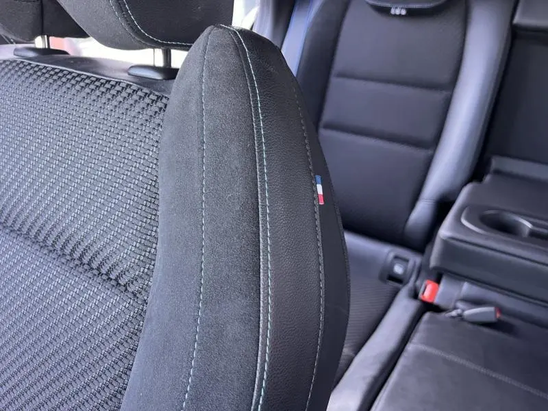 Gros plan sur l'appui-tête avant gauche en tissu carbone et alcantara noir avec surpiqûres bleues et drapeau tricolore Renault.