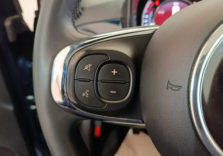 Gros plan sur les commandes du volant cuir de la FIAT 500 Hybrid bleu, avec boutons de volume et reconnaissance vocale.