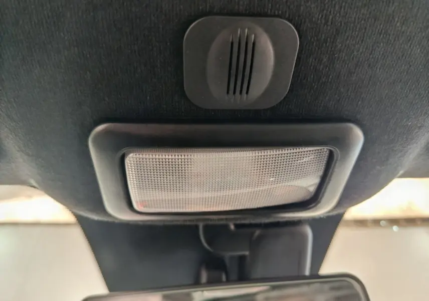 Plafonnier intérieur noir avec haut-parleur intégré, au-dessus du rétroviseur dans une Fiat 500 bleue hybride.