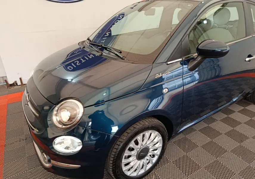 Vue 3/4 avant droite d'une FIAT 500 Dolcevita bleu foncé avec jantes alliage et logo distinctif sur la porte.