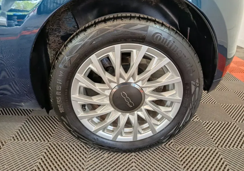 Gros plan sur la roue avant droite d'une FIAT 500 bleu, mettant en valeur la jante argentée au design étoilé.
