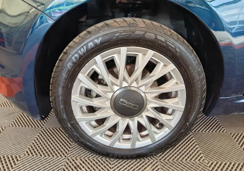 Gros plan sur la roue avant droite d'une FIAT 500 Dolcevita bleue avec jante argentée à rayons fins.