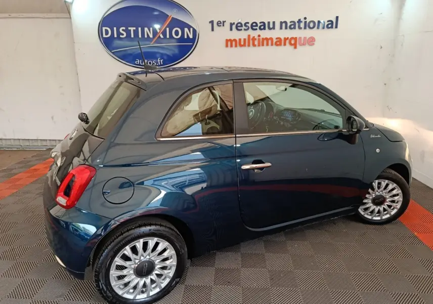 Vue latérale droite d'une FIAT 500 Dolcevita hybride bleu foncé avec jantes alliage et toit noir en intérieur showroom.