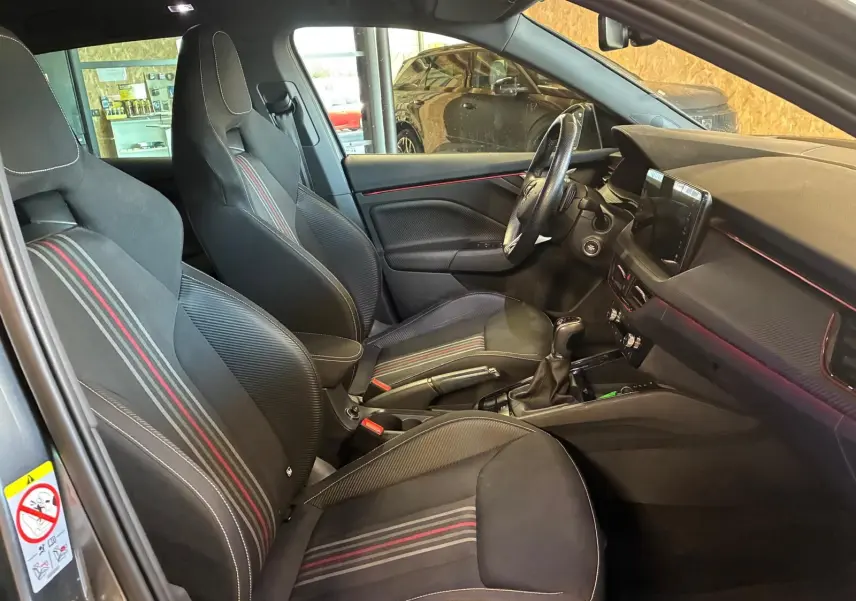 Intérieur de la Skoda Kamiq 2024 en vue latérale gauche, sièges tissu noir avec bandes rouges et tableau de bord moderne.
