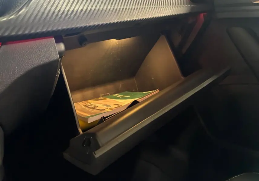 Intérieur du SKODA KAMIQ 2024 gris foncé, vue sur la boîte à gants ouverte avec éclairage intérieur et documents visibles.