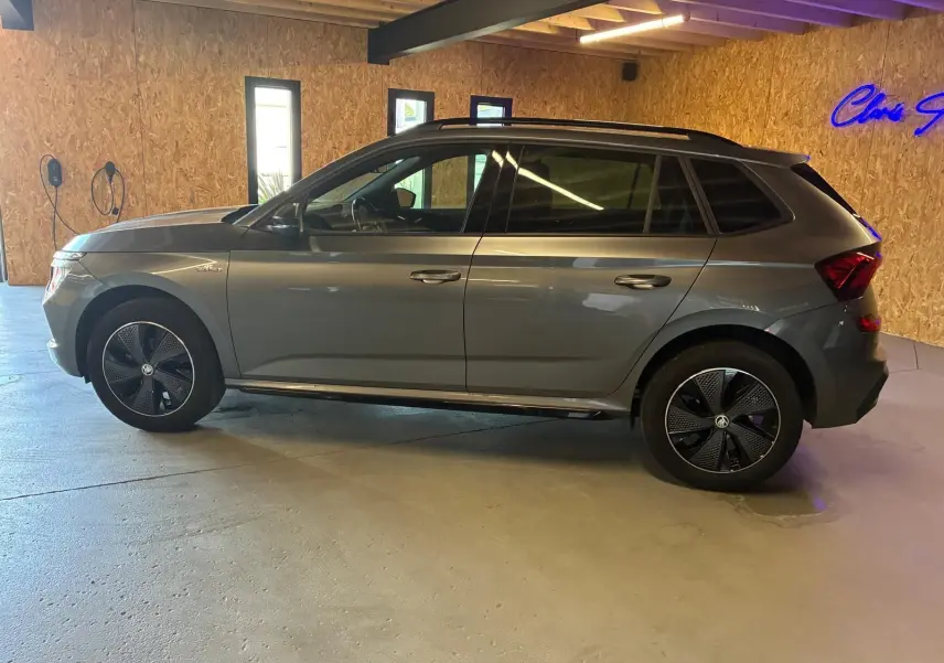 Vue de profil côté gauche d'un Skoda Kamiq gris foncé 2024 en version Monte-Carlo, stationné en intérieur.