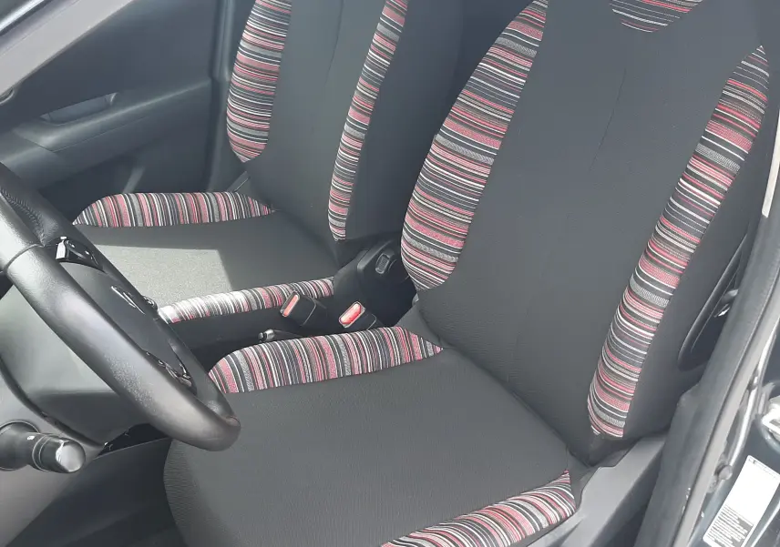 Vue intérieure côté conducteur de la Citroën C1 gris foncé 2019, sièges en tissu noir avec motifs rayés rouges et blancs.