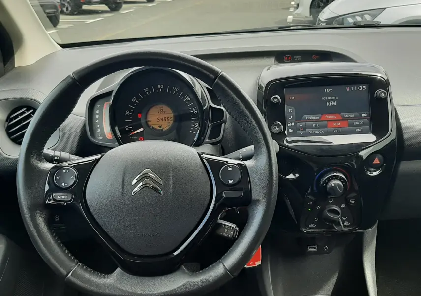 Vue intérieure centrée sur le volant et le tableau de bord d'une Citroën C1 gris foncé avec écran tactile et boîte manuelle.