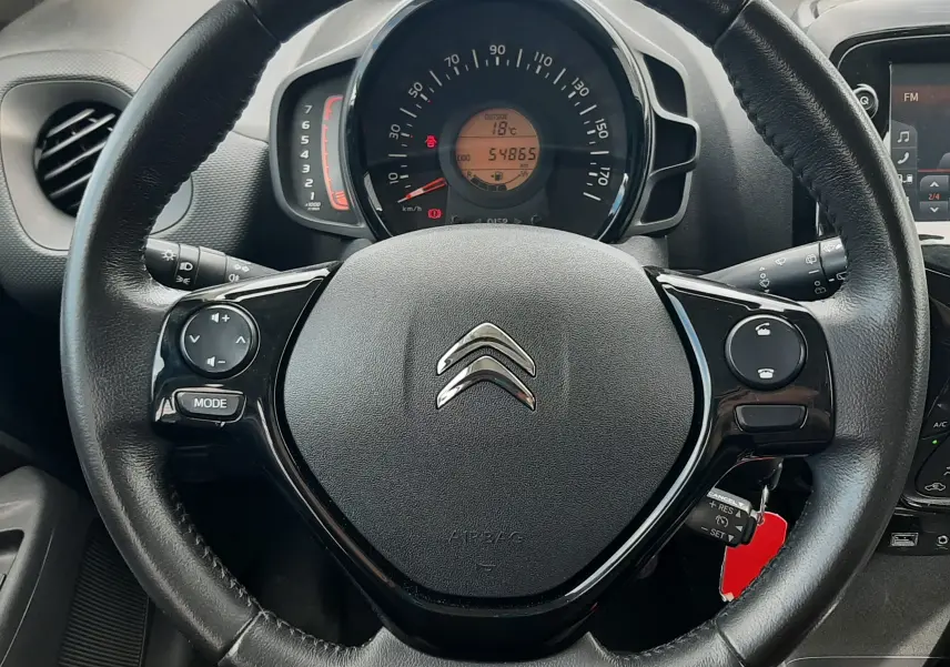 Vue rapprochée du volant noir de la Citroën C1 gris foncé 2019, avec commandes intégrées et tableau de bord visible.