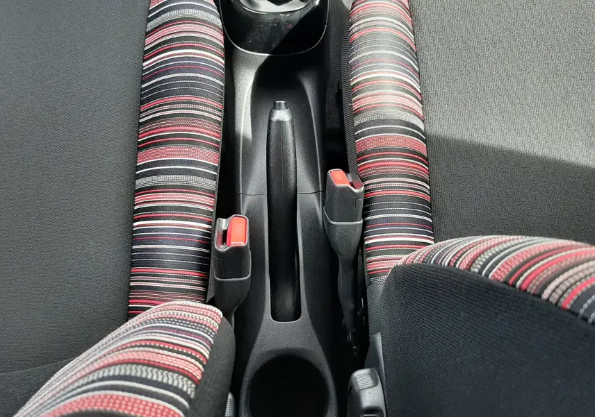 Vue plongeante sur la console centrale et les sièges avant à tissu rayé rouge et noir d'une Citroën C1 gris foncé 2019.