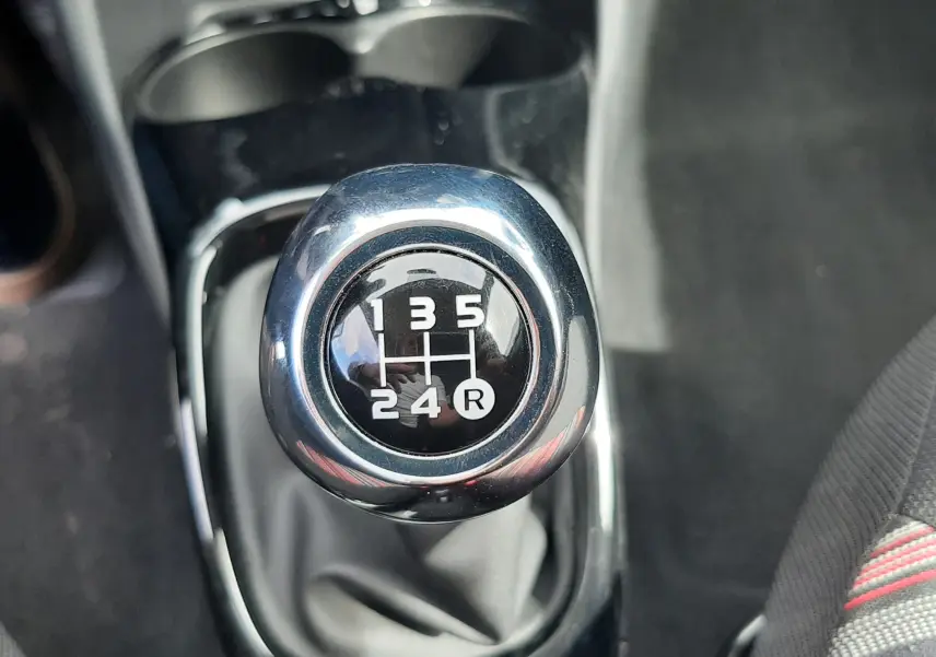 Gros plan sur le levier de vitesses manuel noir et chrome de la Citroën C1 gris foncé, intérieur tissu rayé.