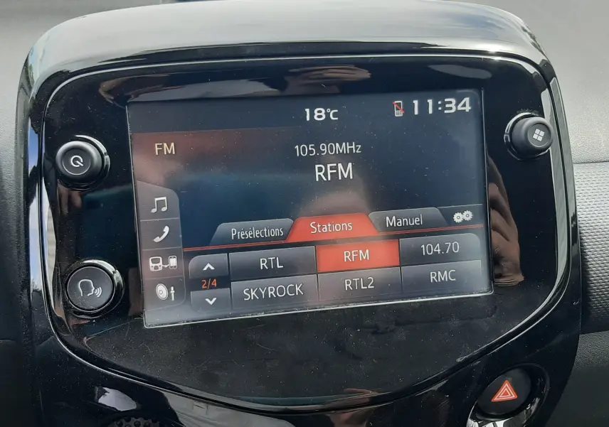 Vue rapprochée de l’écran tactile central noir du tableau de bord d’une Citroën C1 gris foncé, affichant les stations radio FM.