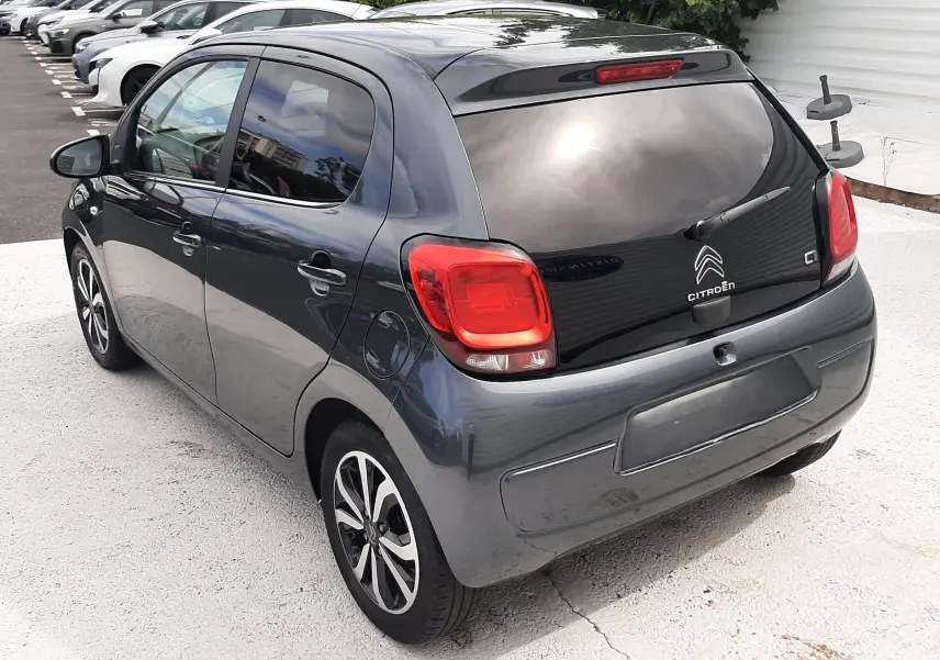 Vue 3/4 arrière droite d'une Citroën C1 gris foncé 5 portes avec feux arrière rouges et jantes bi-ton.