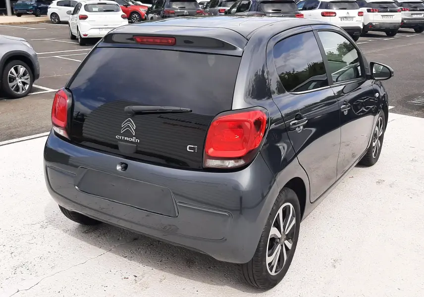 Vue 3/4 arrière droite d'une Citroën C1 gris foncé 5 portes avec vitres arrière teintées et jantes alliage biton.