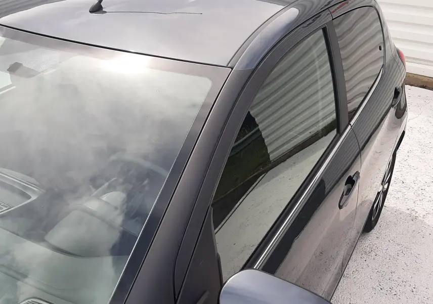 Vue en plongée côté gauche arrière d'une Citroën C1 gris foncé 5 portes avec rétroviseur et vitres teintées.