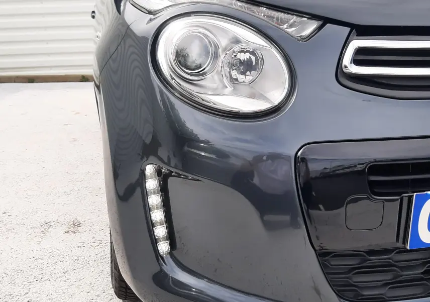 Gros plan sur l’avant gauche d’une Citroën C1 gris foncé 2019, mettant en valeur le phare rond et la bande LED verticale.