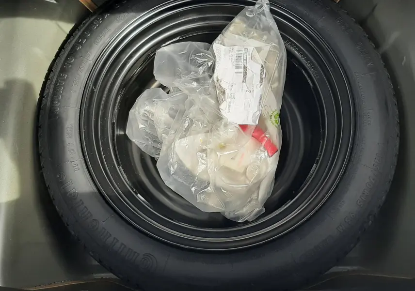 Roue de secours noire dans le coffre d'une Citroën C1 gris foncé, version essence 2019, avec sac plastique dessus.