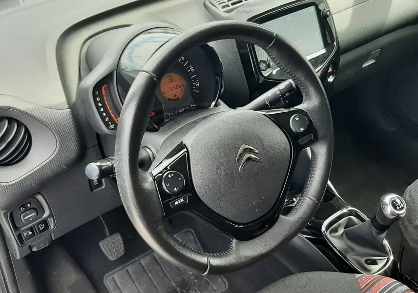 Vue intérieure centrée sur le volant noir et le tableau de bord digital de la Citroën C1 2019, avec levier de vitesses manuel visible.