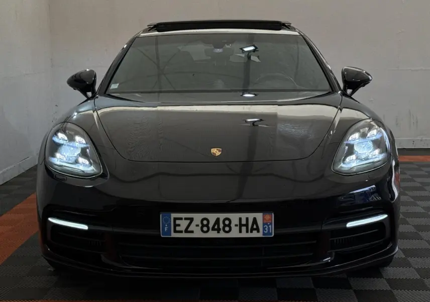 Vue frontale d'une Porsche Panamera 4 E-Hybrid Sport Turismo noire avec phares LED allumés et plaque d'immatriculation française.