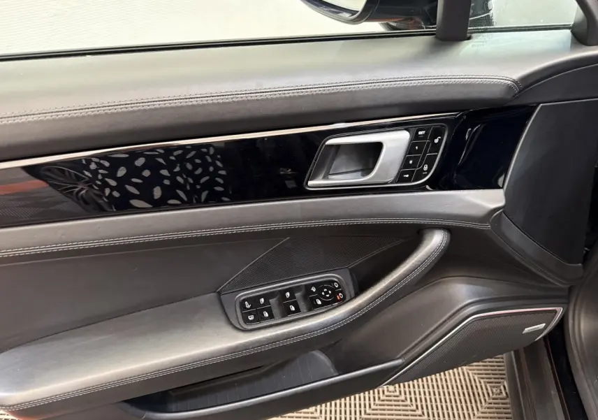 Vue intérieure côté gauche de la porte avant noire de la Porsche Panamera 4 E-Hybrid avec commandes électriques et finition cuir.
