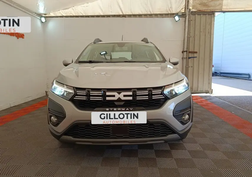 Vue frontale d'une Dacia Sandero Expression gris clair avec phares LED allumés dans un garage.