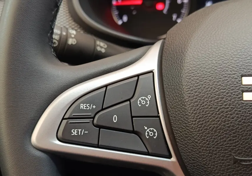 Gros plan sur le volant cuir synthétique gris d'une Dacia Sandero 2023, avec commandes du régulateur de vitesse visibles.