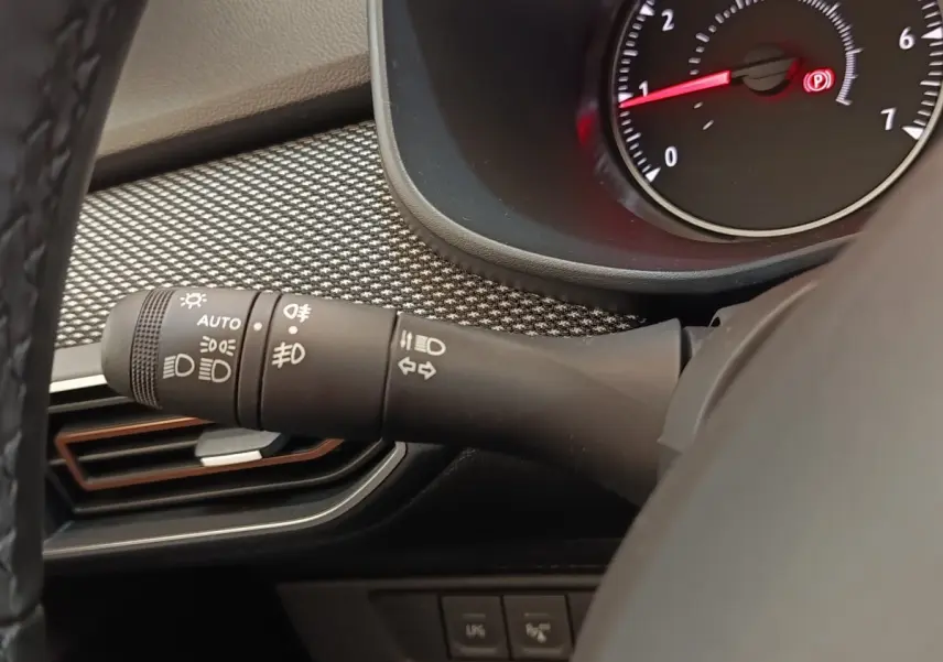 Gros plan sur la manette des feux à gauche du volant cuir synthétique dans l’habitacle gris clair du Dacia Sandero 2023.