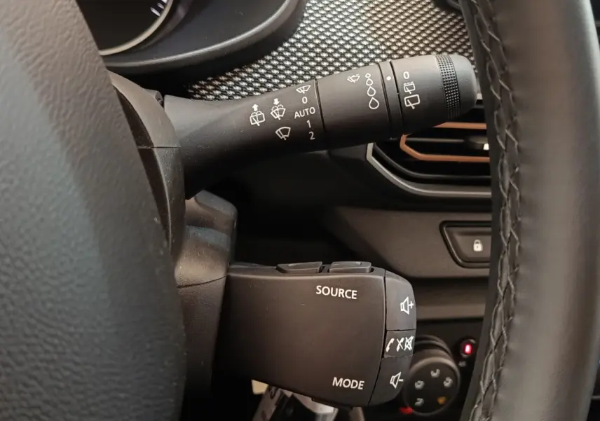 Gros plan sur la commande multifonctions à gauche du volant cuir noir dans l’habitacle d’une Dacia Sandero gris clair 2023.