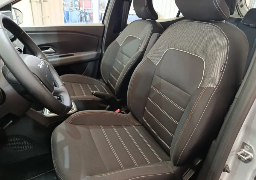 Vue intérieure côté conducteur de la Dacia Sandero Expression EGO-G 100 2023, sièges tissu noir avec surpiqûres contrastées.