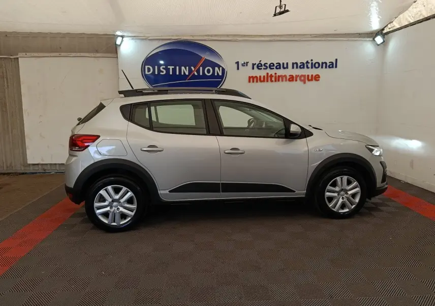 Vue de profil côté gauche d'une Dacia Sandero gris clair 2023 avec protections noires et jantes alliage.