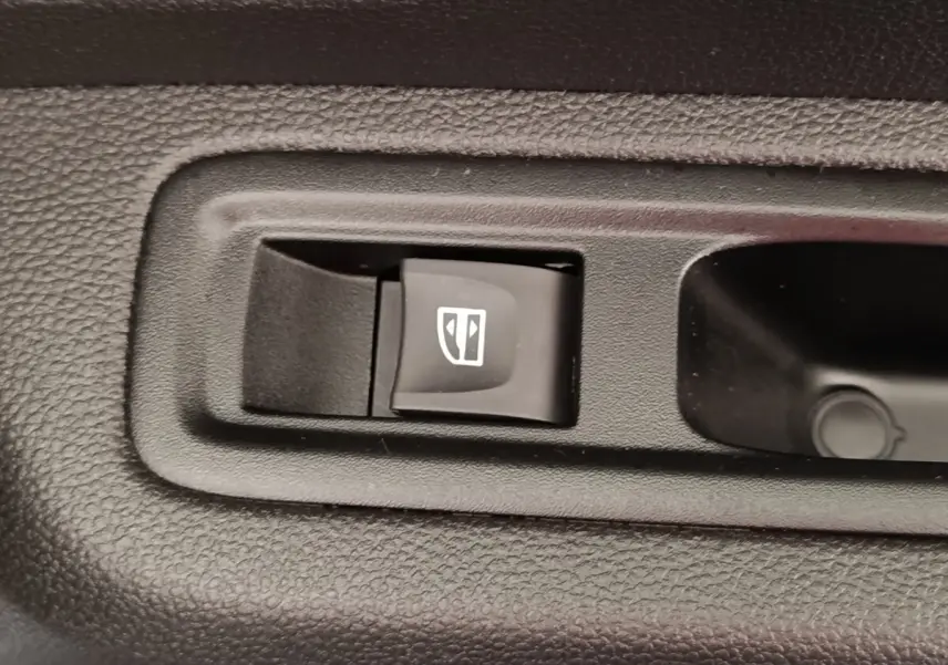 Gros plan sur le bouton de commande électrique de la fenêtre côté conducteur dans l’habitacle noir de la Dacia Sandero gris clair.