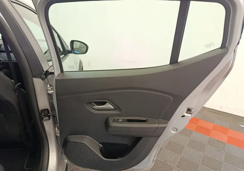 Vue intérieure de la porte arrière gauche gris clair d'une Dacia Sandero Expression EGO-G 2023, avec poignée et commande de vitre.
