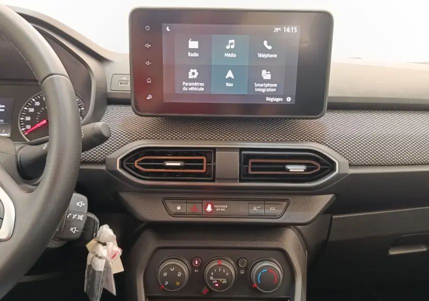 Vue intérieure frontale du tableau de bord de la Dacia Sandero gris clair, avec écran tactile multifonctions et aérateurs hexagonaux.
