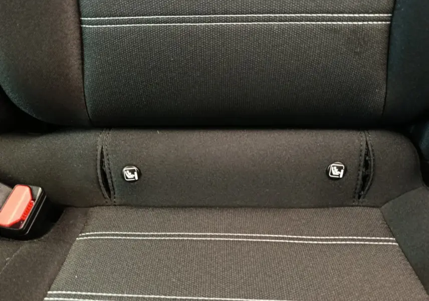 Gros plan sur la banquette arrière noire avec surpiqûres blanches et fixations Isofix visibles dans une Dacia Sandero gris clair.
