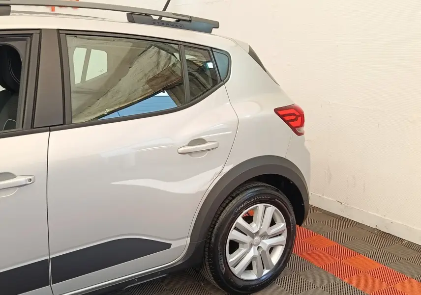 Vue côté droit arrière d'une Dacia Sandero Expression gris clair avec jante alliage et barres de toit Stepway.