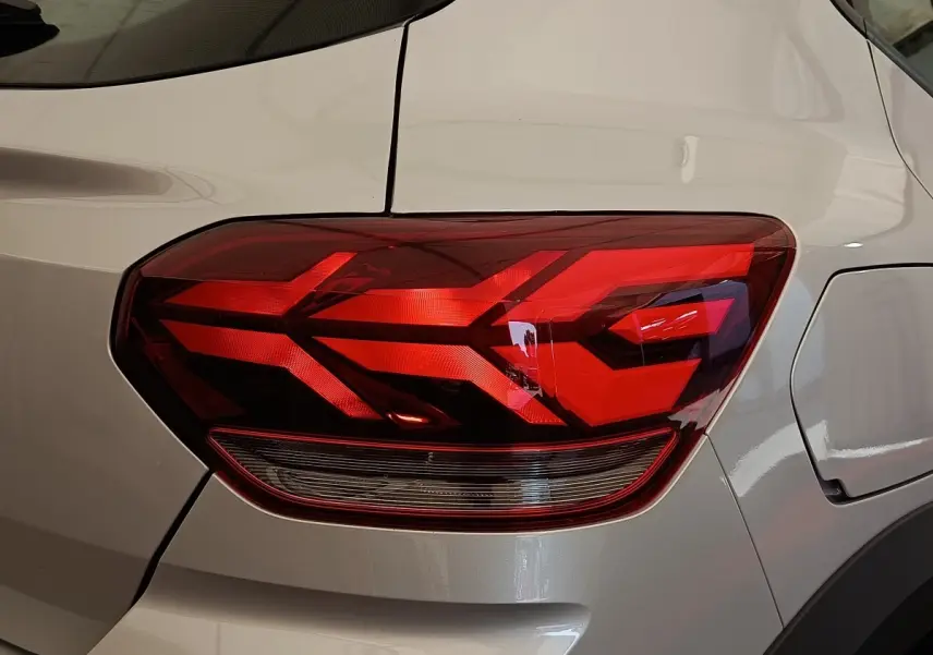Gros plan sur le feu arrière droit rouge d’une Dacia Sandero gris clair 2023, avec la trappe à carburant visible.