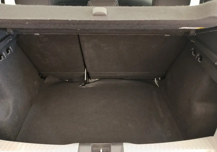 Coffre ouvert vu de l'arrière d'une Dacia Sandero gris clair 2023, montrant l'espace de chargement avec banquette rabattue.
