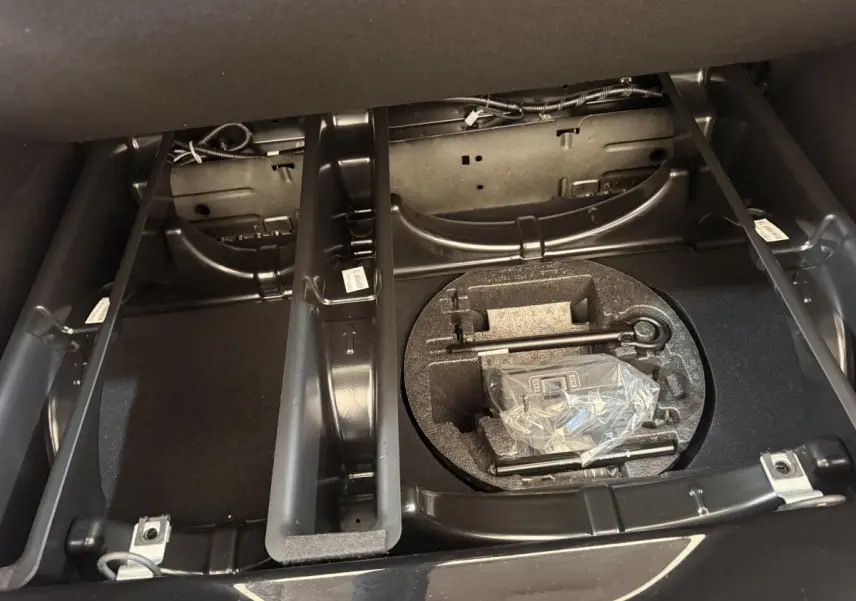 Vue intérieure du coffre de la Renault ZOE noire 2024, montrant le rangement sous plancher avec outils et espace de chargement.