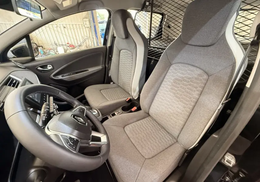 Vue intérieure côté conducteur de la Renault ZOE noire 2024, volant cuir synthétique et sièges gris avec séparation grillagée.