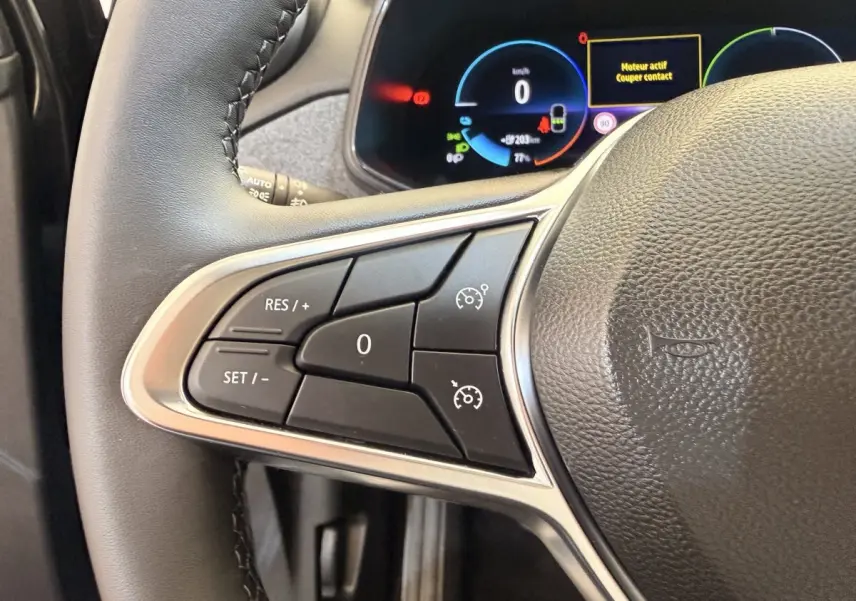 Gros plan sur le volant cuir synthétique noir de la Renault ZOE 2024 avec commandes multifonctions et tableau de bord digital.